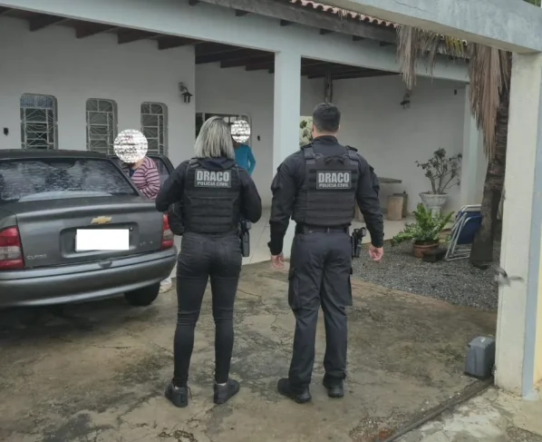 Foto de oficiais da Draco conversando com moradores de uma residência