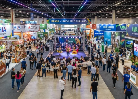 Feira de turismo estruturada com estandes institucionais, apresentações culturais e público circulando em pavilhão amplo