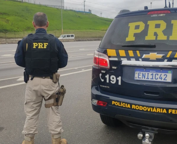 Oficial da PRF ao lado de viatura