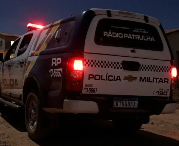 Viatura policial parada em rua de distrito rural com residências simples ao fundo durante a noite