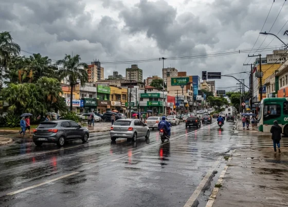 Rua urbana de Cuiabá com asfalto molhado por chuva passageira sob céu nublado