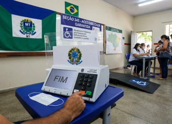 Urna eletrônica em seção eleitoral com sinalização de acessibilidade e bandeira institucional
